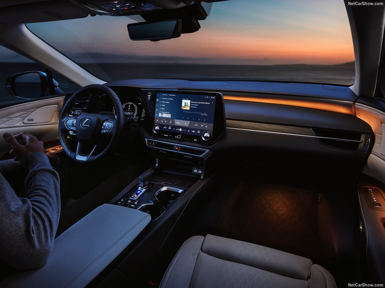 Wnętrze Lexus RX 350h Prestige z widokiem na deskę rozdzielczą i ekranem, eleganckie oświetlenie, zachód słońca za oknem.